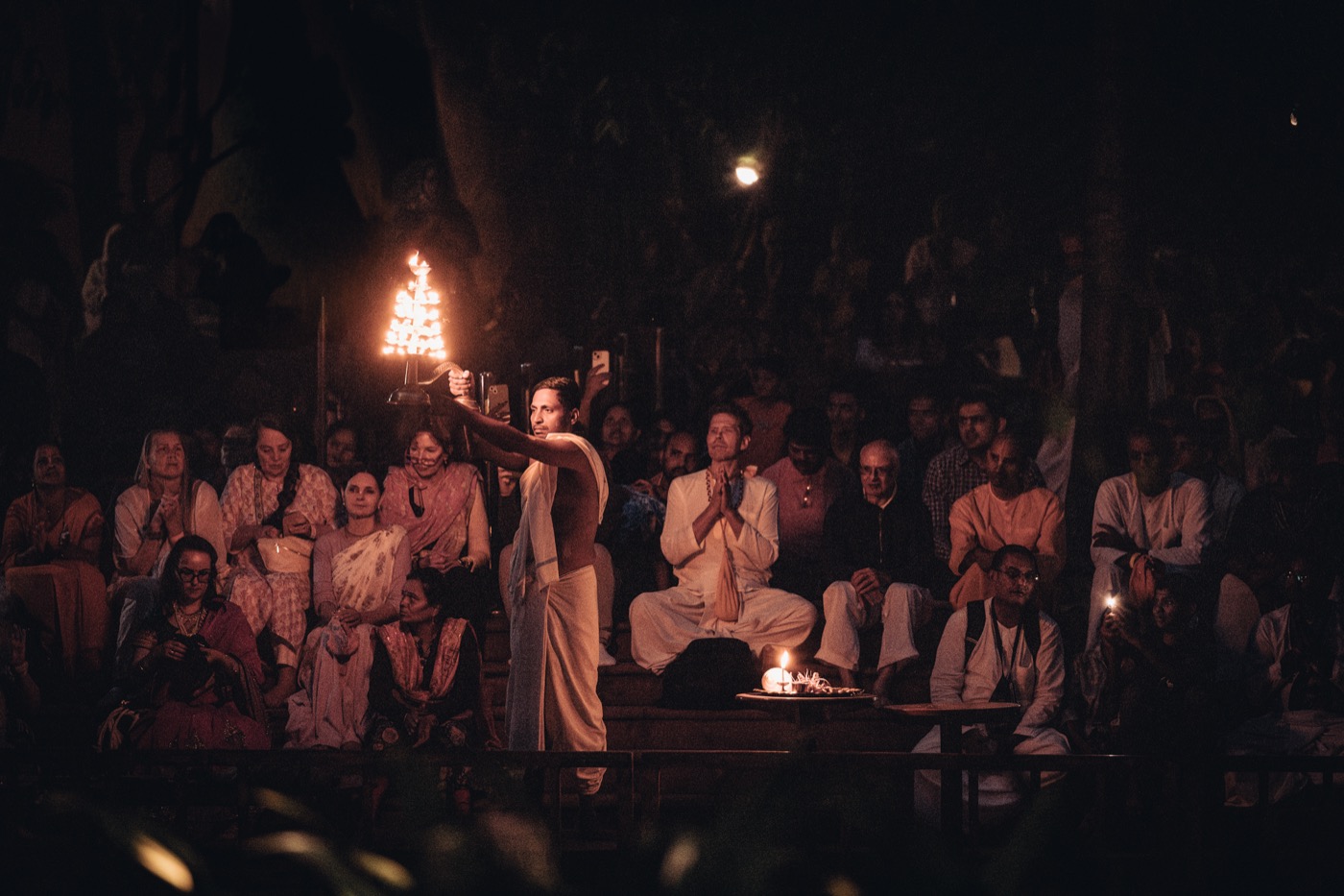 A devotee offering arati before a gathered congregation at dusk